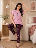 Woman wearing pink t-shirt and purple patterned pants in a cozy living room.