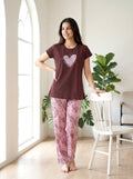 Woman wearing a brown t-shirt with a heart design and pink patterned pants in a bright room.