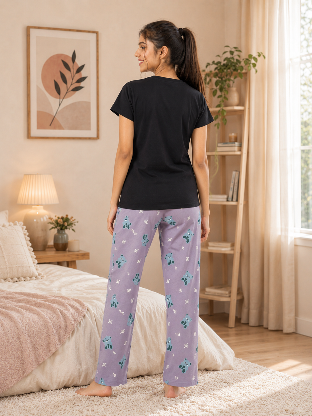 Woman wearing black t-shirt and purple floral pajama pants in a bedroom.