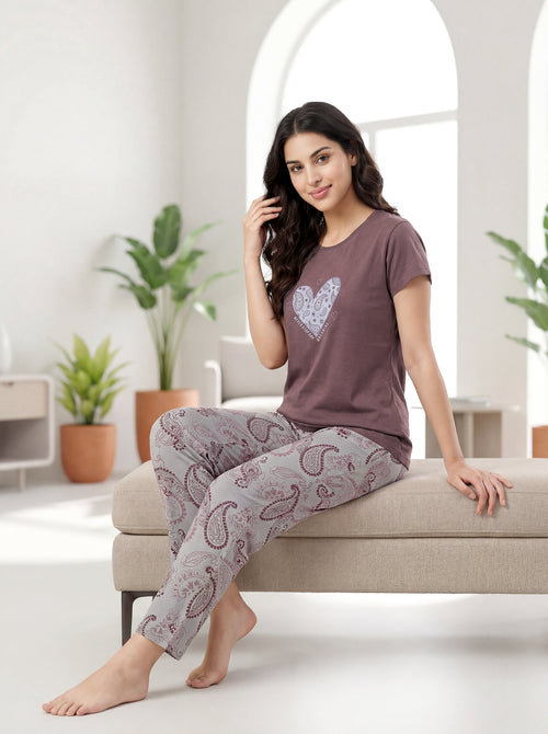 Woman wearing a matching pajama set sitting on a couch in a bright living room.