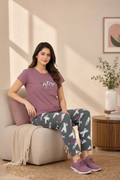 Woman sitting on a couch wearing a purple t-shirt and patterned pants in a cozy living room.
