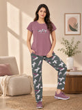Woman wearing a purple t-shirt and patterned pants in a living room.
