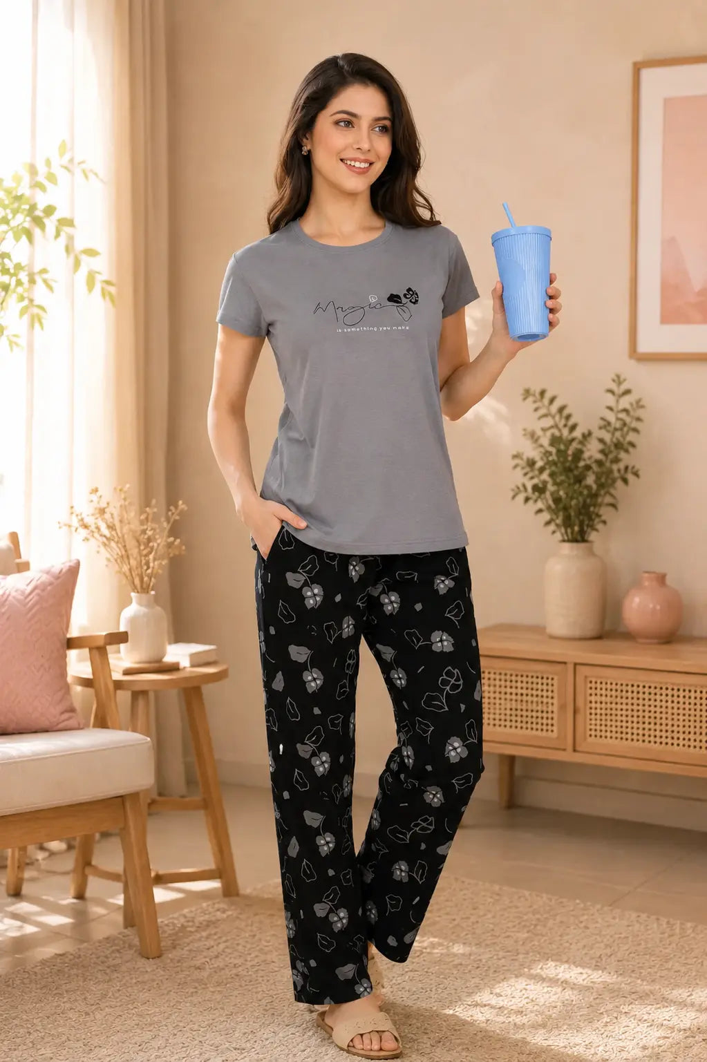 Woman in gray t-shirt and black patterned pants holding a blue cup in a cozy living room.