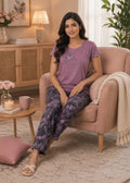 Woman sitting on a pink armchair wearing a purple t-shirt and floral pants in a cozy living room.