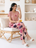 Woman in pink floral pajama set sitting on a chair, holding a phone and a glass.