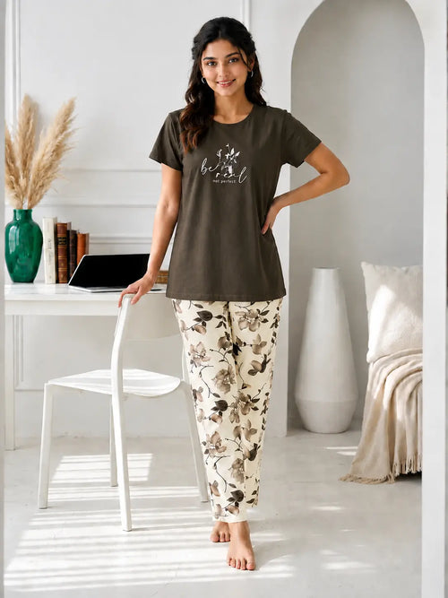 Woman wearing a brown t-shirt and floral pants in a bright room.
