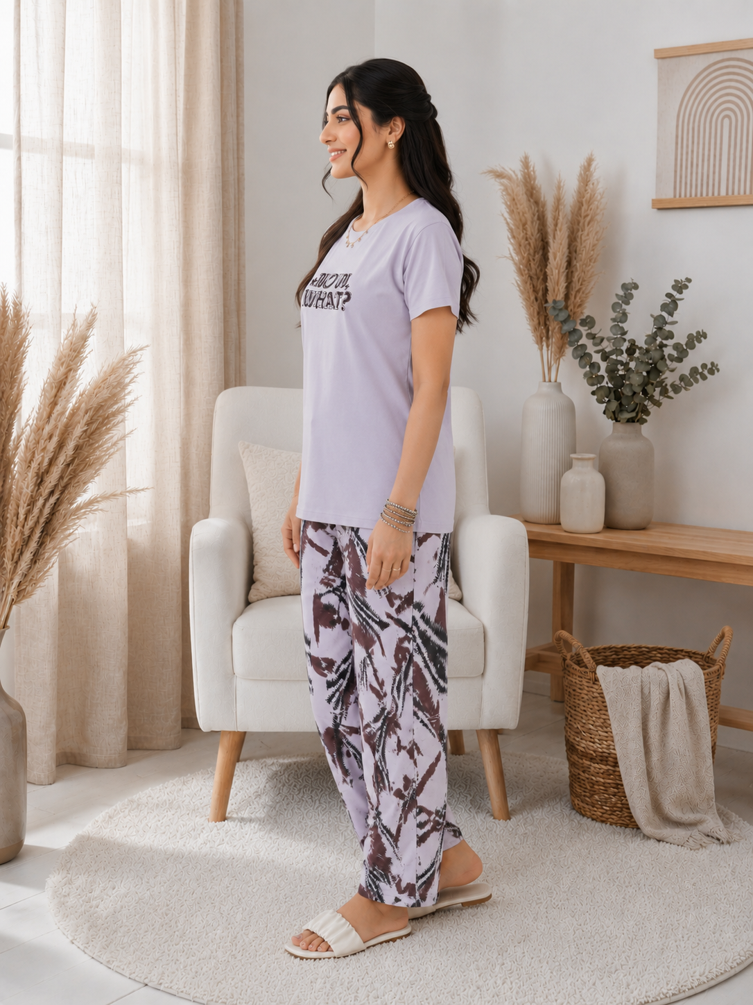 Woman in a light purple t-shirt and patterned pants standing in a bright living room.