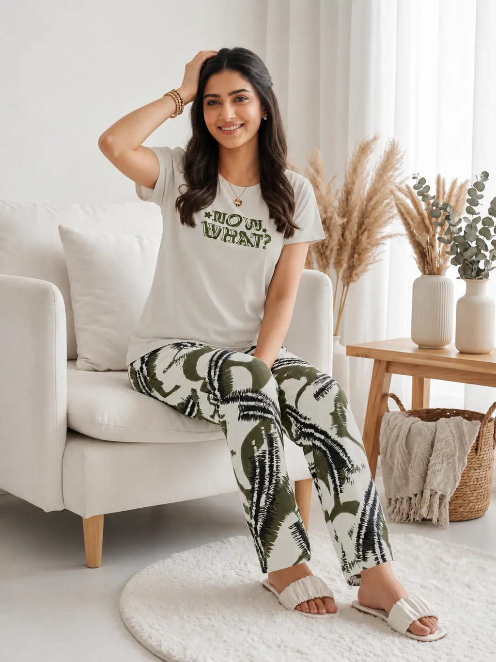 Woman sitting on a white couch wearing a white t-shirt and patterned pants in a bright living room.