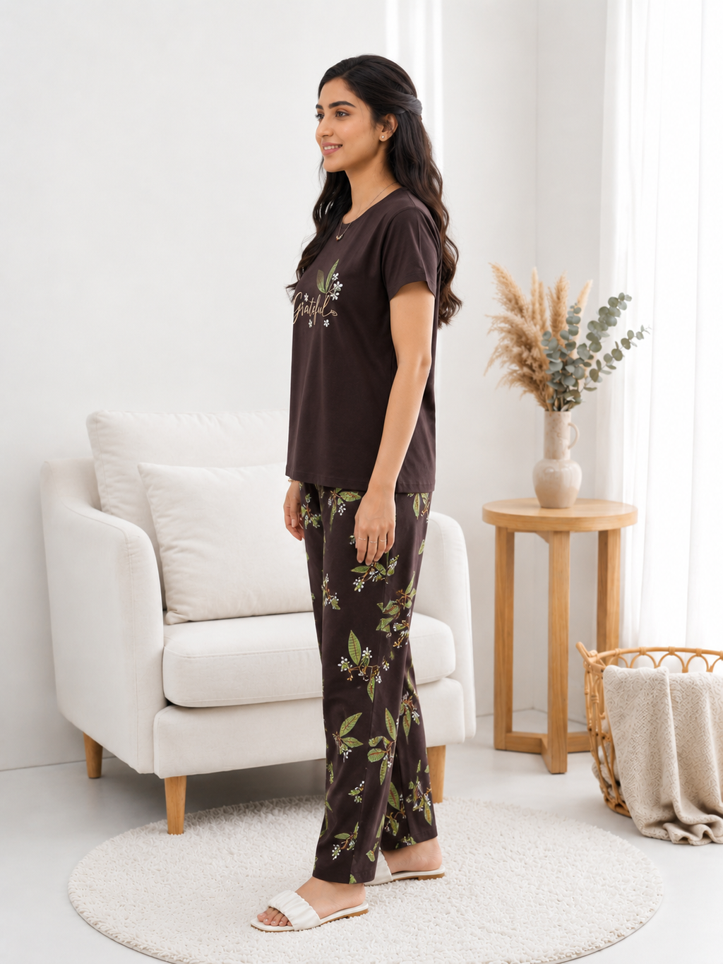Woman wearing a brown t-shirt and floral pants in a living room setting.