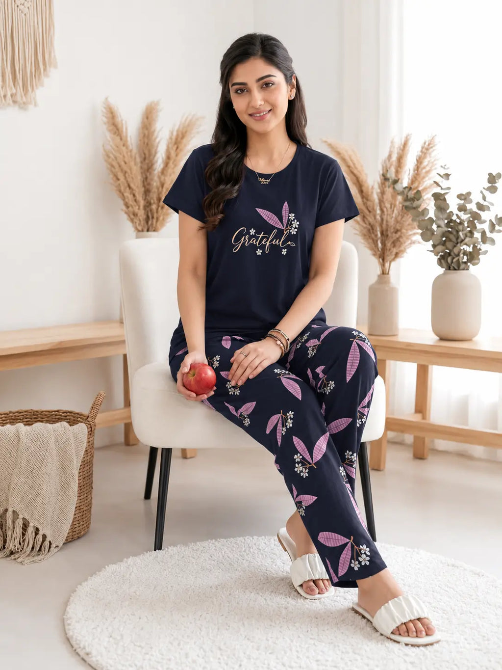 Woman sitting in a cozy room wearing a navy blue 'Grateful' t-shirt and floral pants.