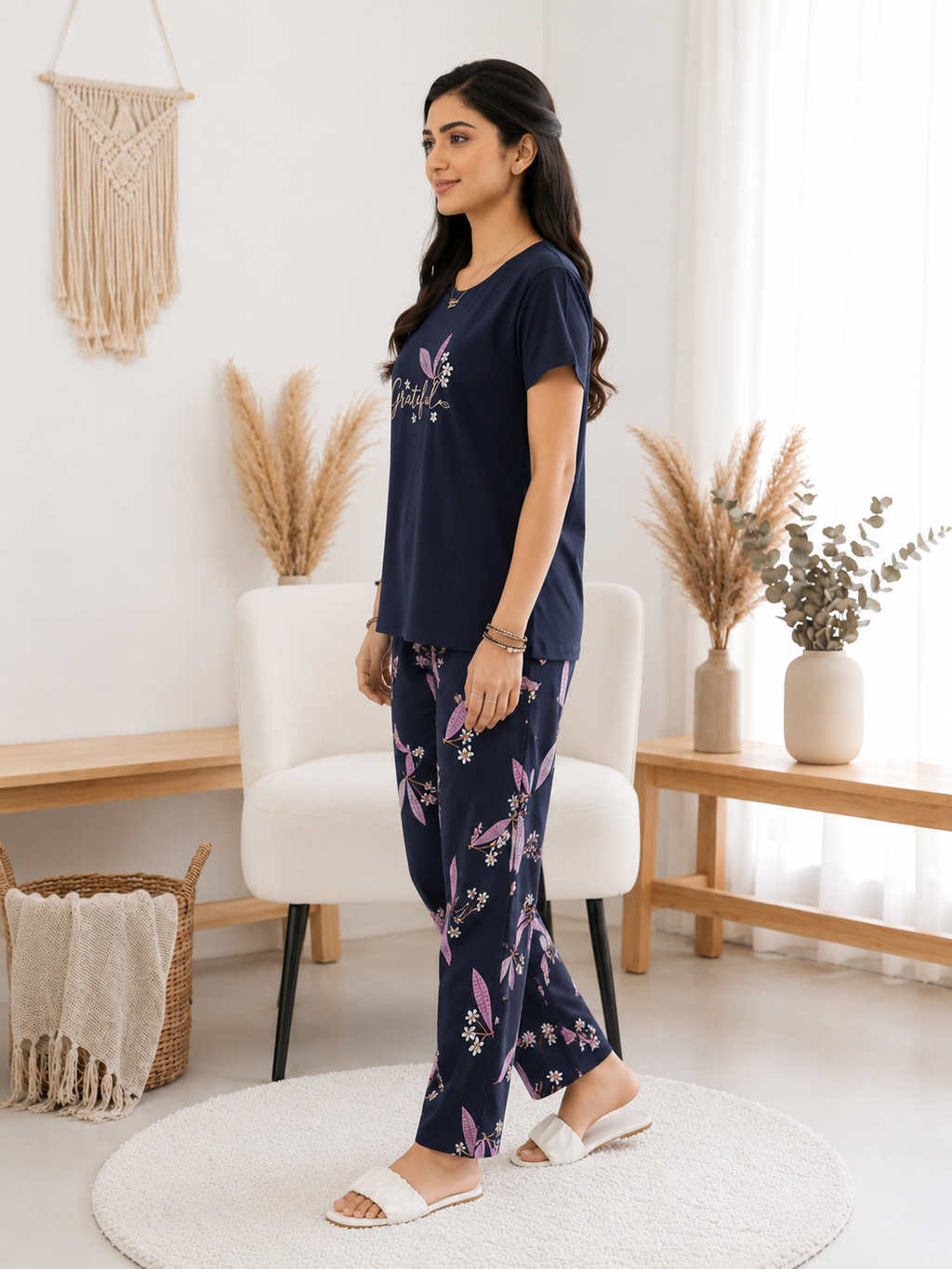 Woman wearing a navy blue pajama set with floral patterns in a bright living room.