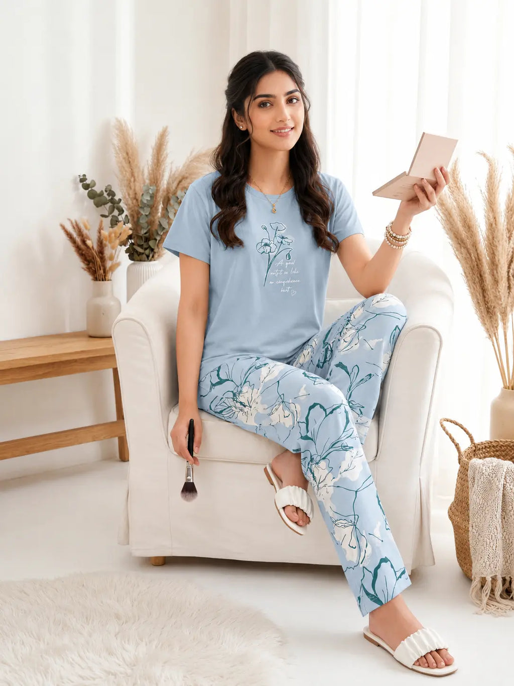 Woman sitting on a chair wearing a light blue t-shirt and floral pants, holding a tablet.