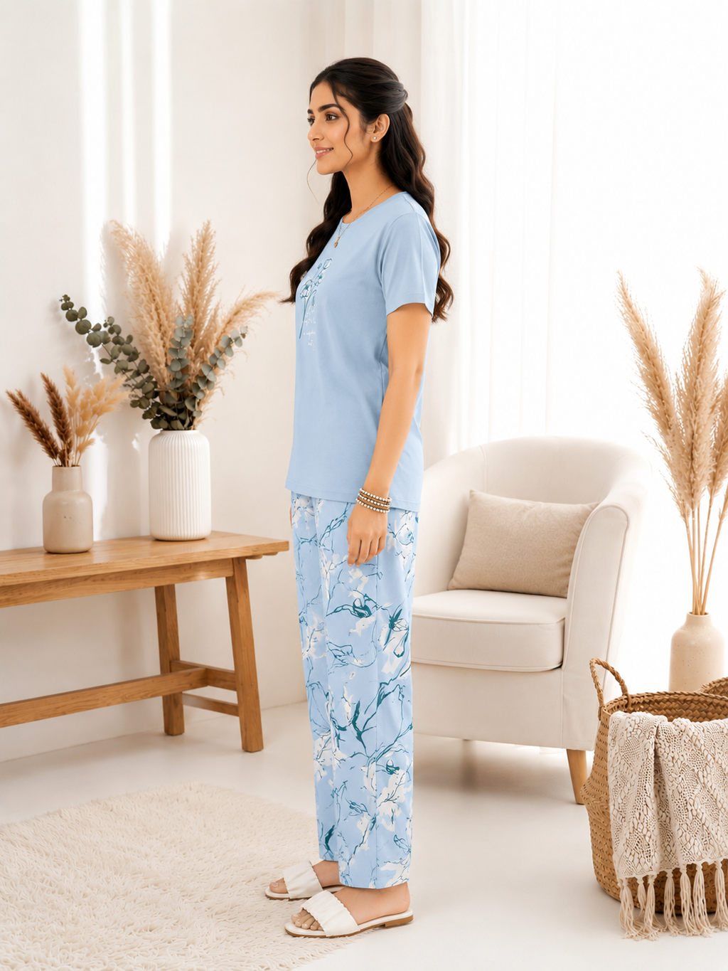 Woman in light blue top and floral pants standing in a bright living room.