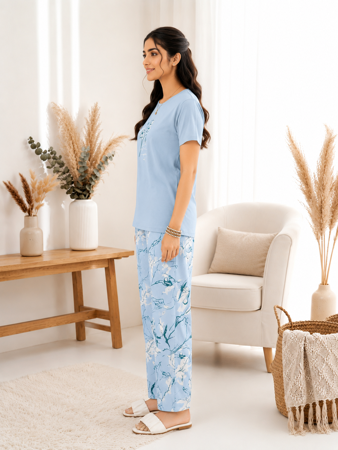 Woman in light blue top and floral pants standing in a bright living room.
