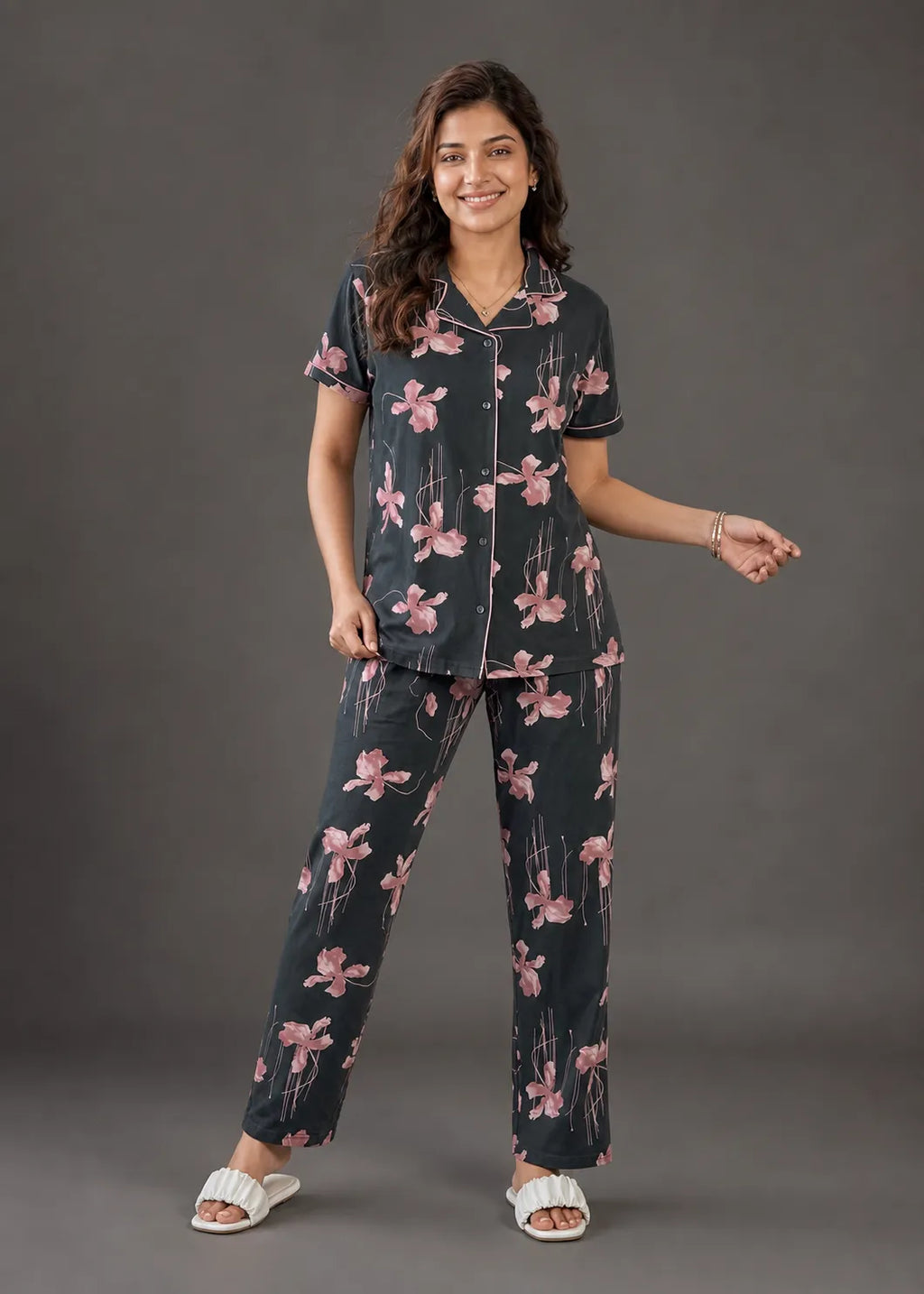 A woman modeling a two-piece pajama set featuring a dark gray base with a pink floral print, standing against a solid dark gray studio background.