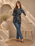 Woman wearing a black floral top and blue jeans standing in a room with a vase and chair.