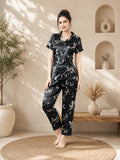 Woman wearing a black floral pajama set in a sunlit room with plants and a wooden shelf.