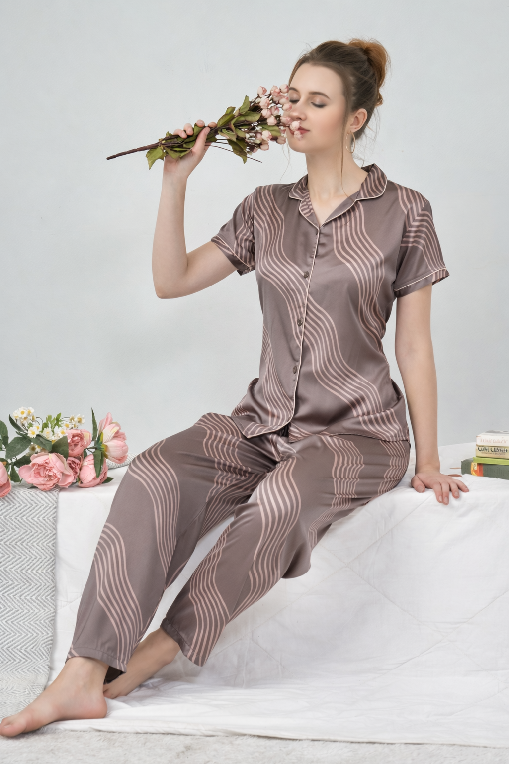 Woman wearing a brown patterned pajama set holding flowers on a white background