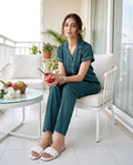 Woman in teal pajamas sitting on a chair holding an apple on a balcony.