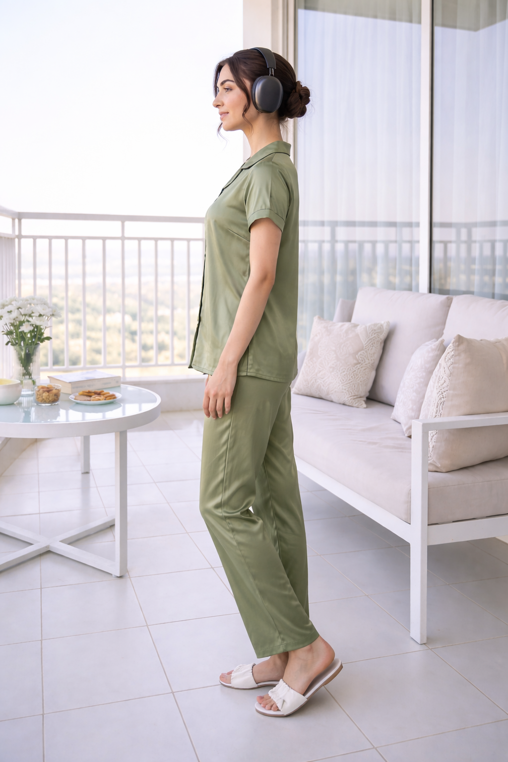 Woman in green outfit standing on a balcony with white furniture and plants.
