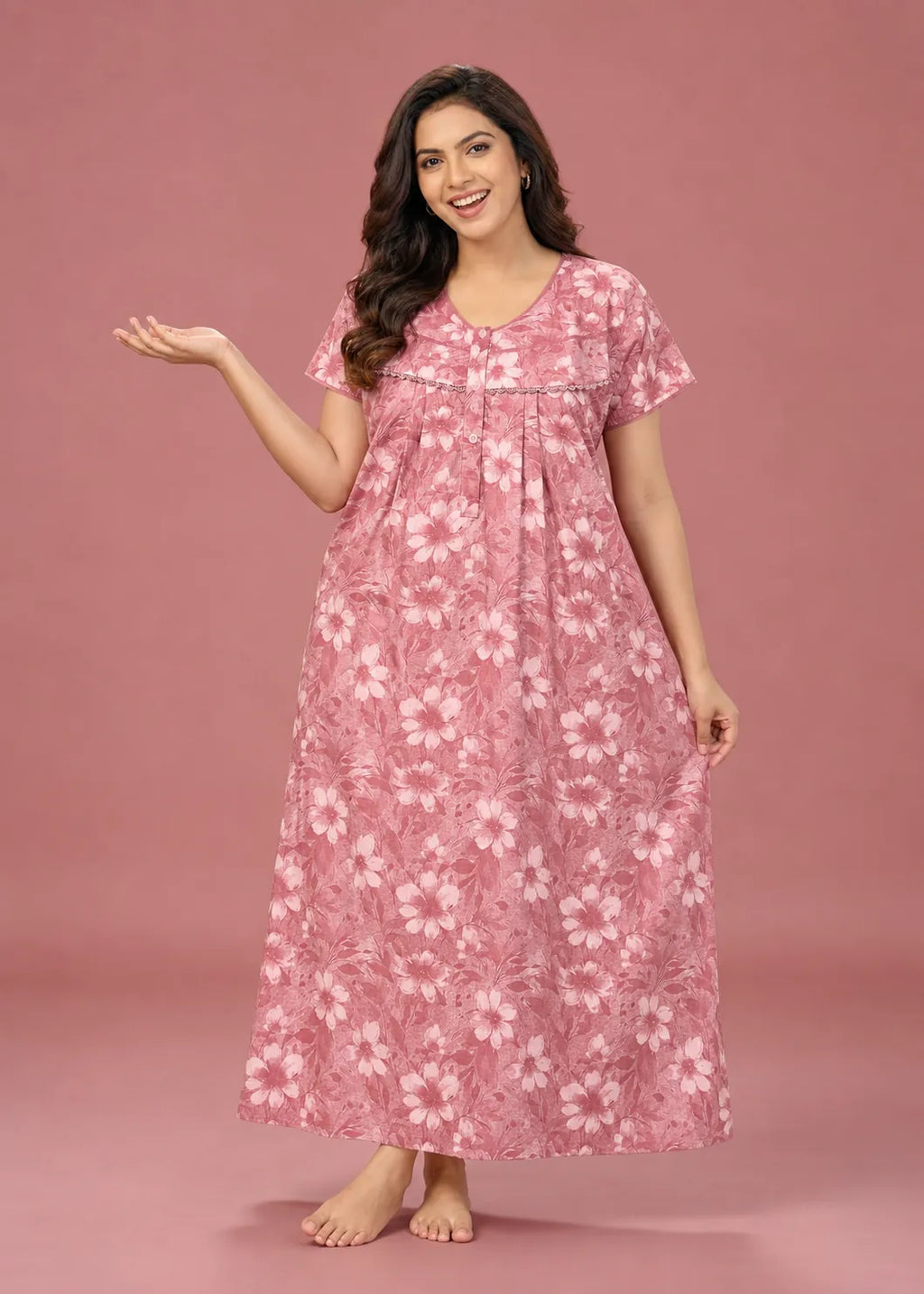 A woman modeling a pink floral nightgown with a white hibiscus flower pattern, standing against a solid pink studio backdrop.