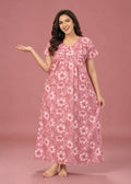 A woman modeling a pink floral nightgown with a white hibiscus flower pattern, standing against a solid pink studio backdrop.