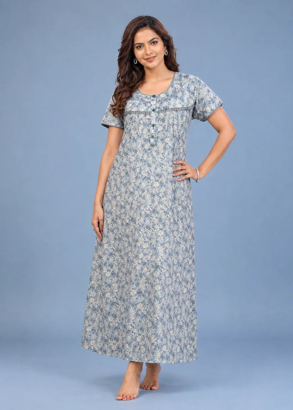 A woman modeling a short-sleeve, floor-length floral nightgown or maxi dress in a light blue and white floral print against a solid blue studio background.