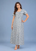 A woman modeling a short-sleeve, floor-length floral nightgown or maxi dress in a light blue and white floral print against a solid blue studio background.