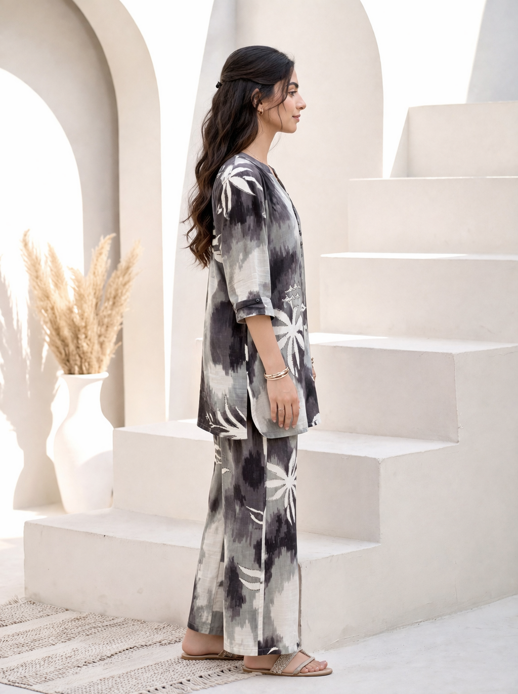 Woman in a black and white tie-dye outfit standing on a staircase with a neutral background