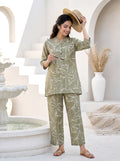 Woman in a green patterned outfit standing in a decorative outdoor setting with arches and a fountain.