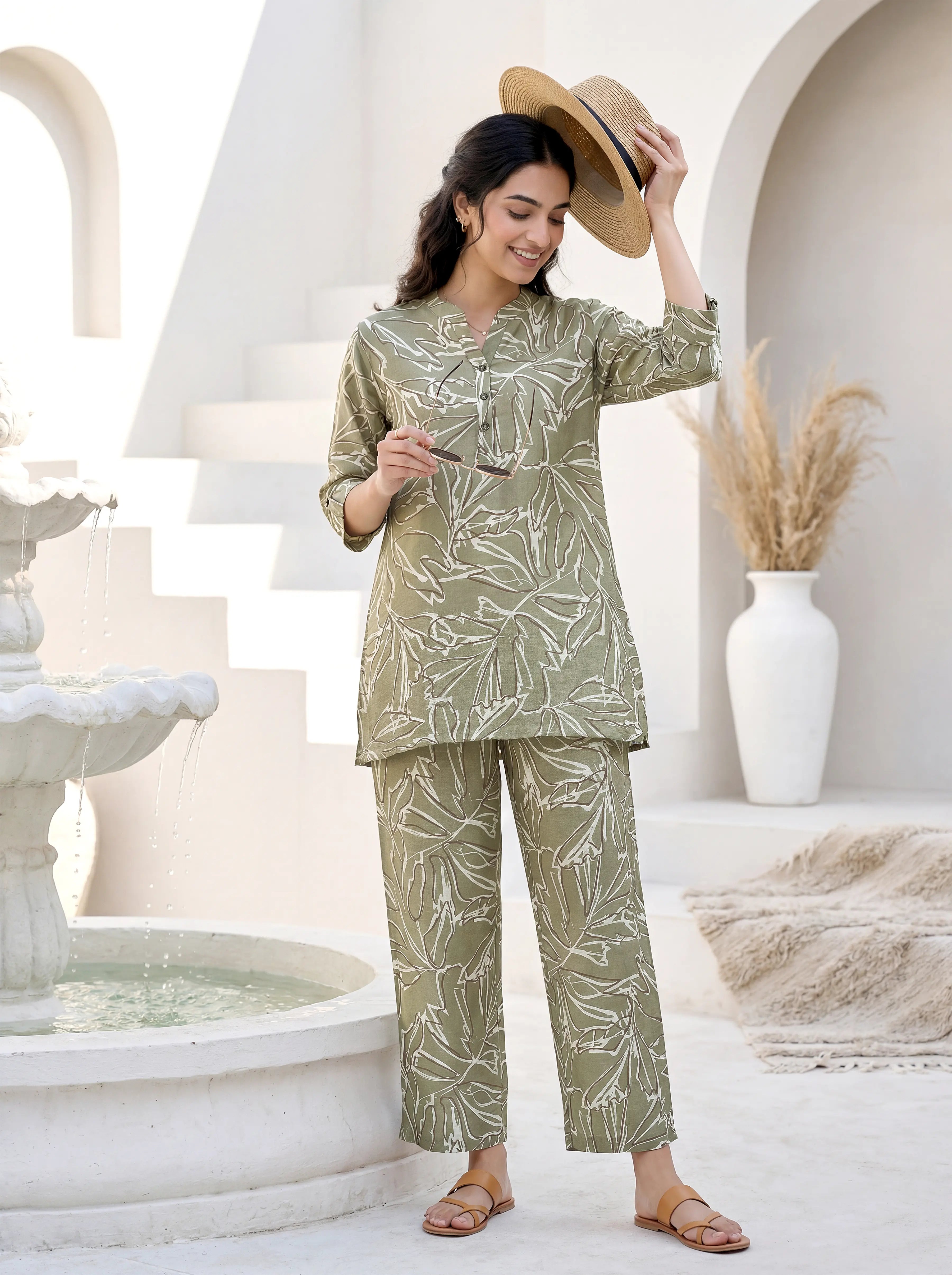 Woman in a green patterned outfit standing in a decorative outdoor setting with arches and a fountain.
