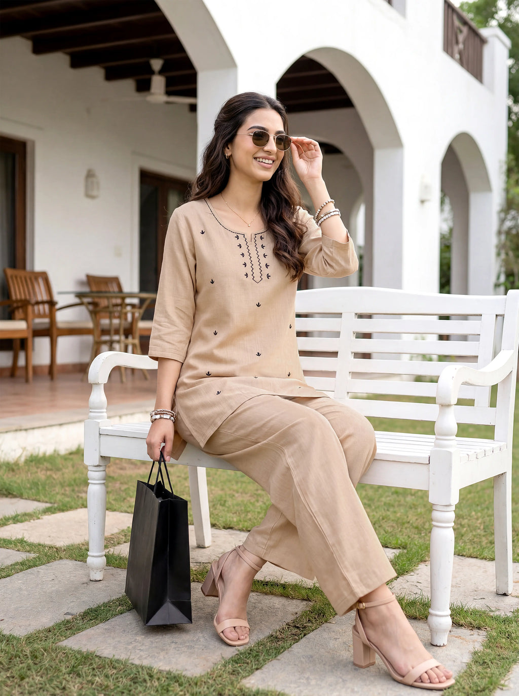 Woman in beige outfit sitting on a white bench outdoors