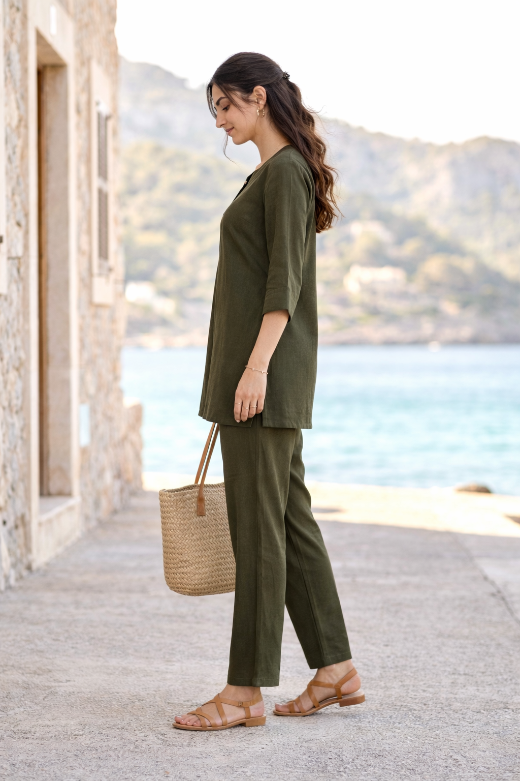 Woman in olive green outfit with a woven bag by a coastal setting