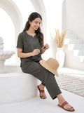 Woman sitting on a white bench wearing a green outfit with a straw hat, holding a phone.