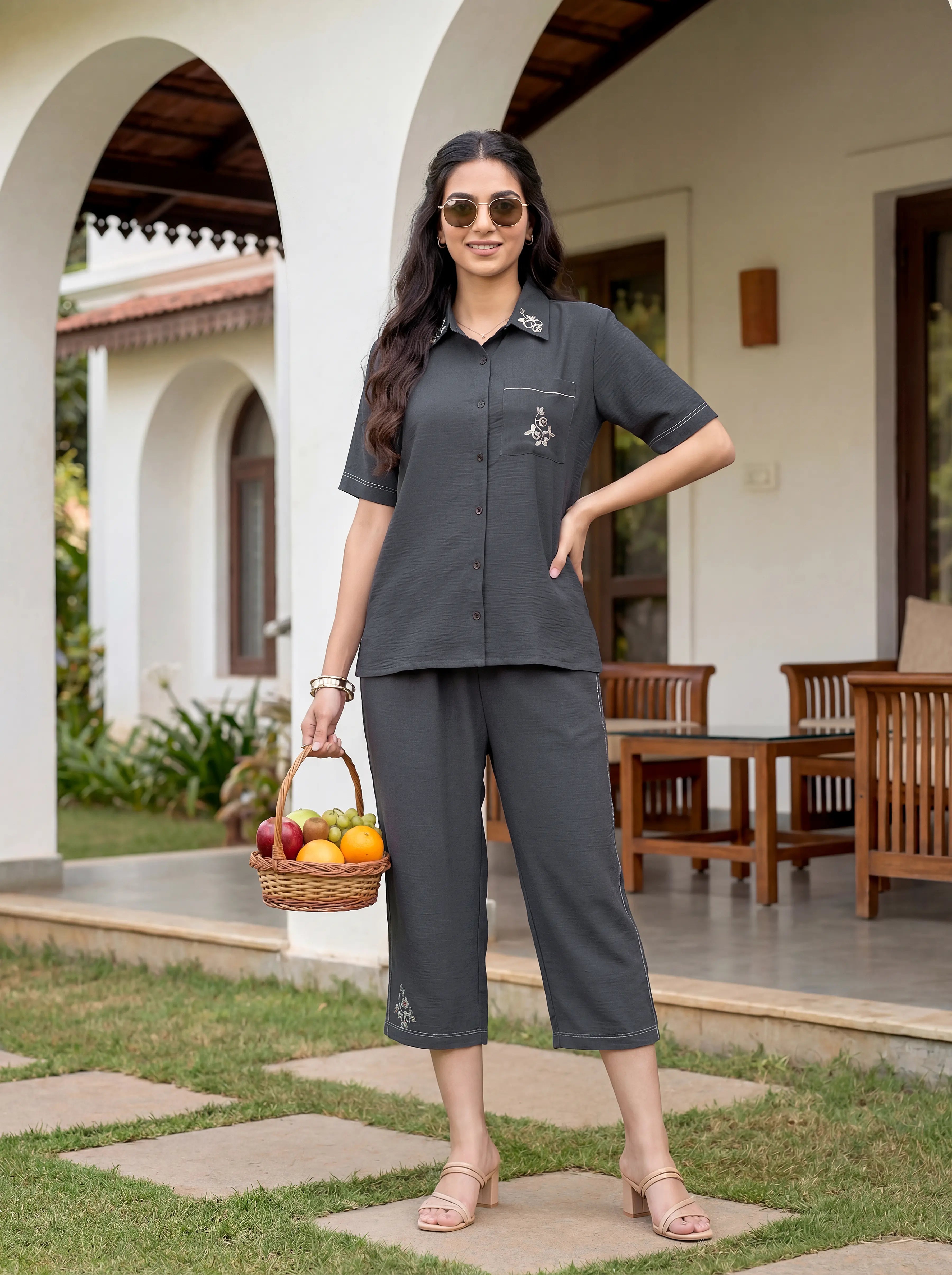 Woman in a gray outfit holding a basket of fruits in front of a house.